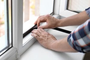 Young man putting sealing foam tape on window indoors